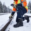 Worker in safety vest wearing JHB06 heated boots while working on snowy railroad tracks