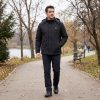 JHJ02B Heated Jacket - Worn View (Outdoors) Man walking in a winter park wearing JHJ02B black heated jacket
